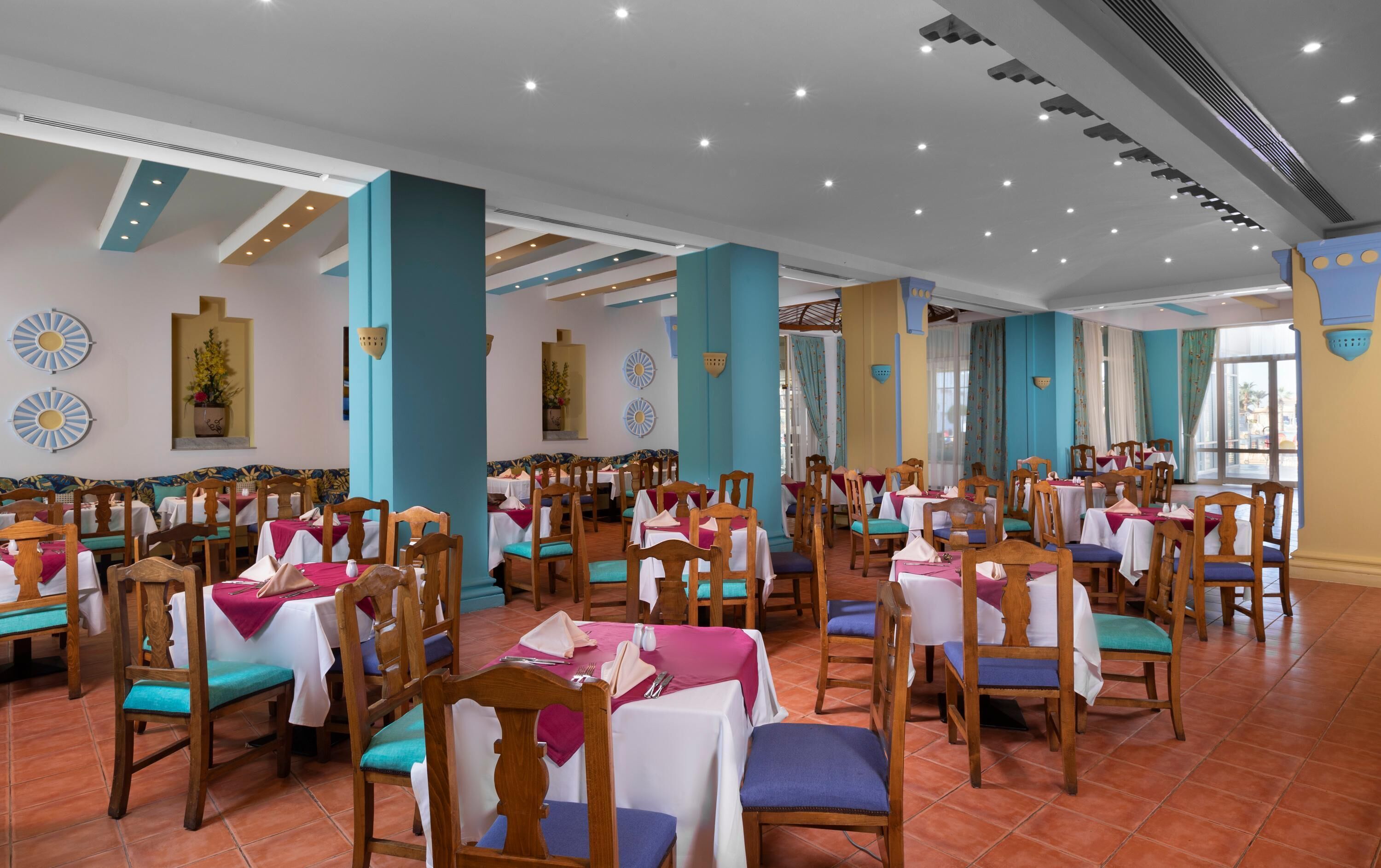 A spacious dining area with multiple tables and chairs, high ceilings with recessed lighting, and decorative wall elements.