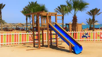 Kids can play on the beachside playground with a blue slide surrounded by a colorful fence.