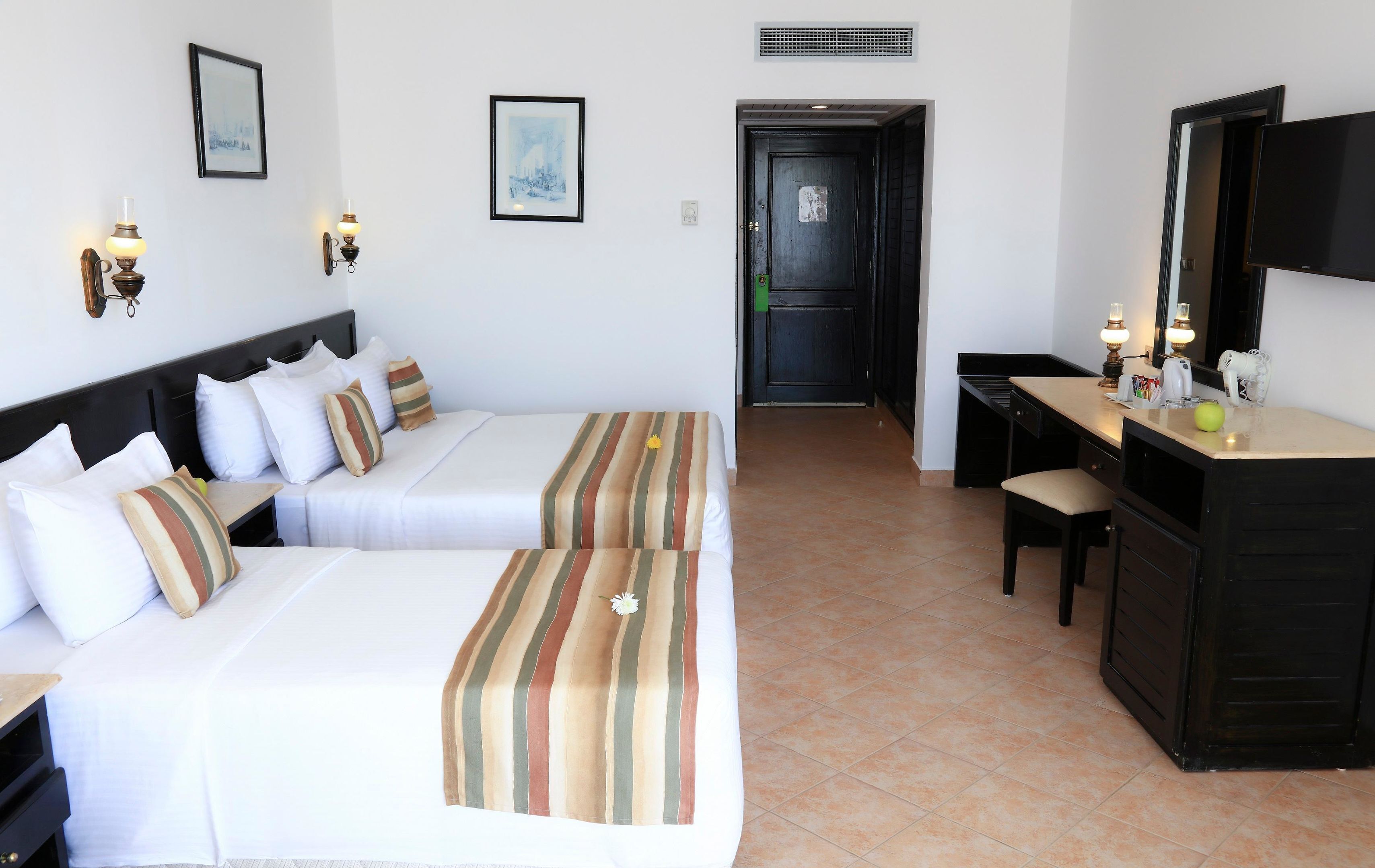 A hotel room with two beds, a desk, a chair, a television, and a door leading to another room.