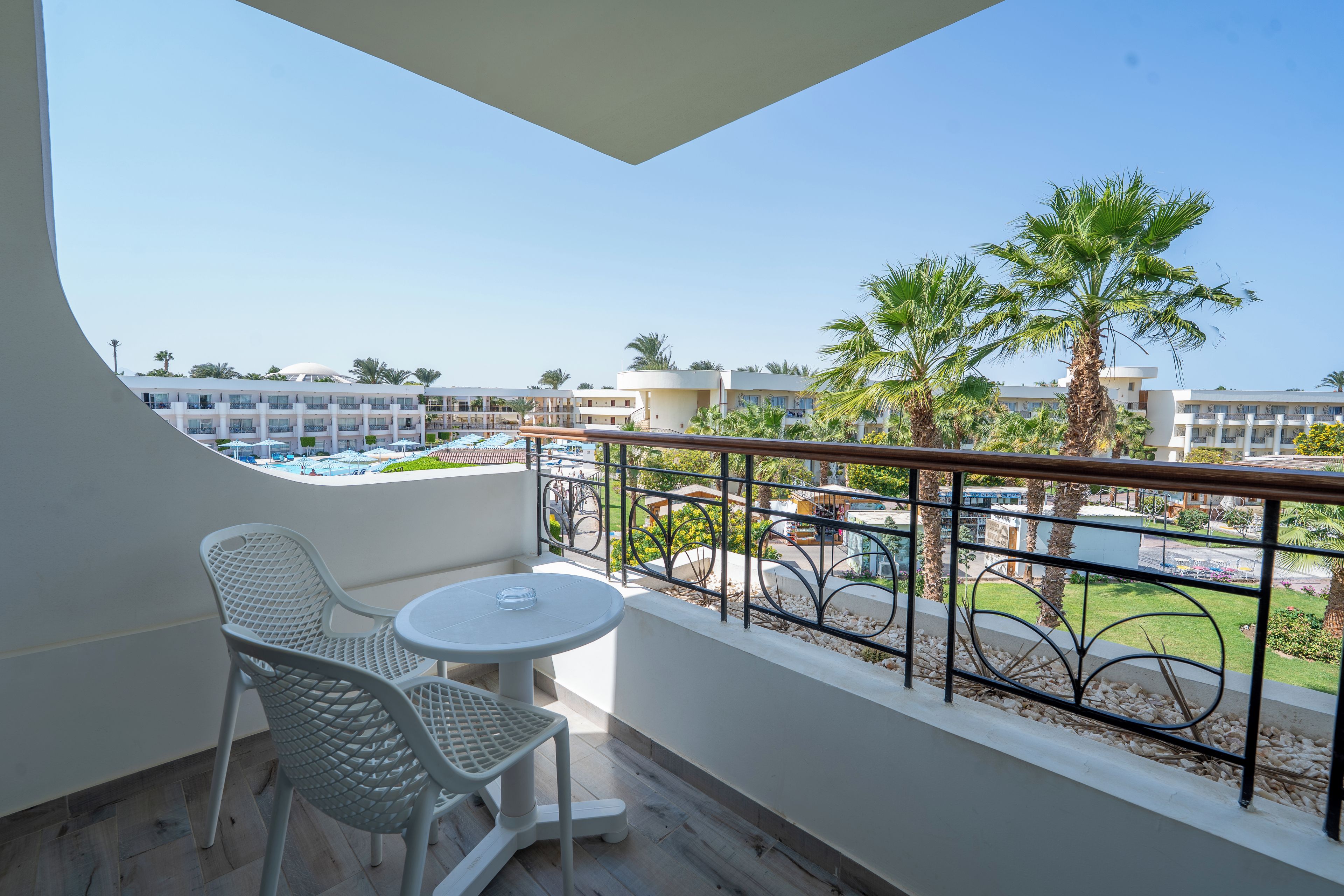 A balcony with a white table and chairs, a pool view, and a railing with decorative elements.