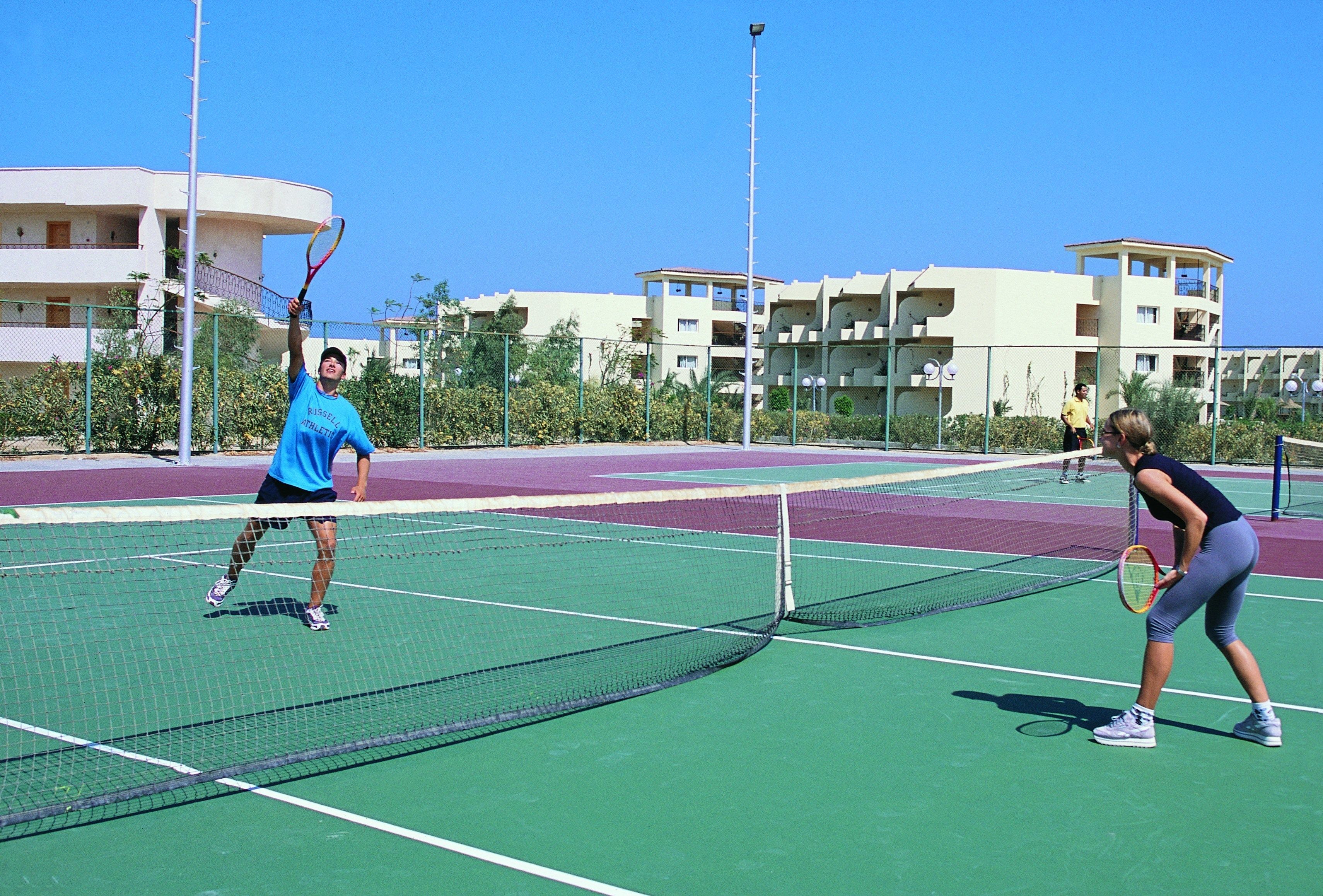 A tennis court with a net in the middle, surrounded by a fence.