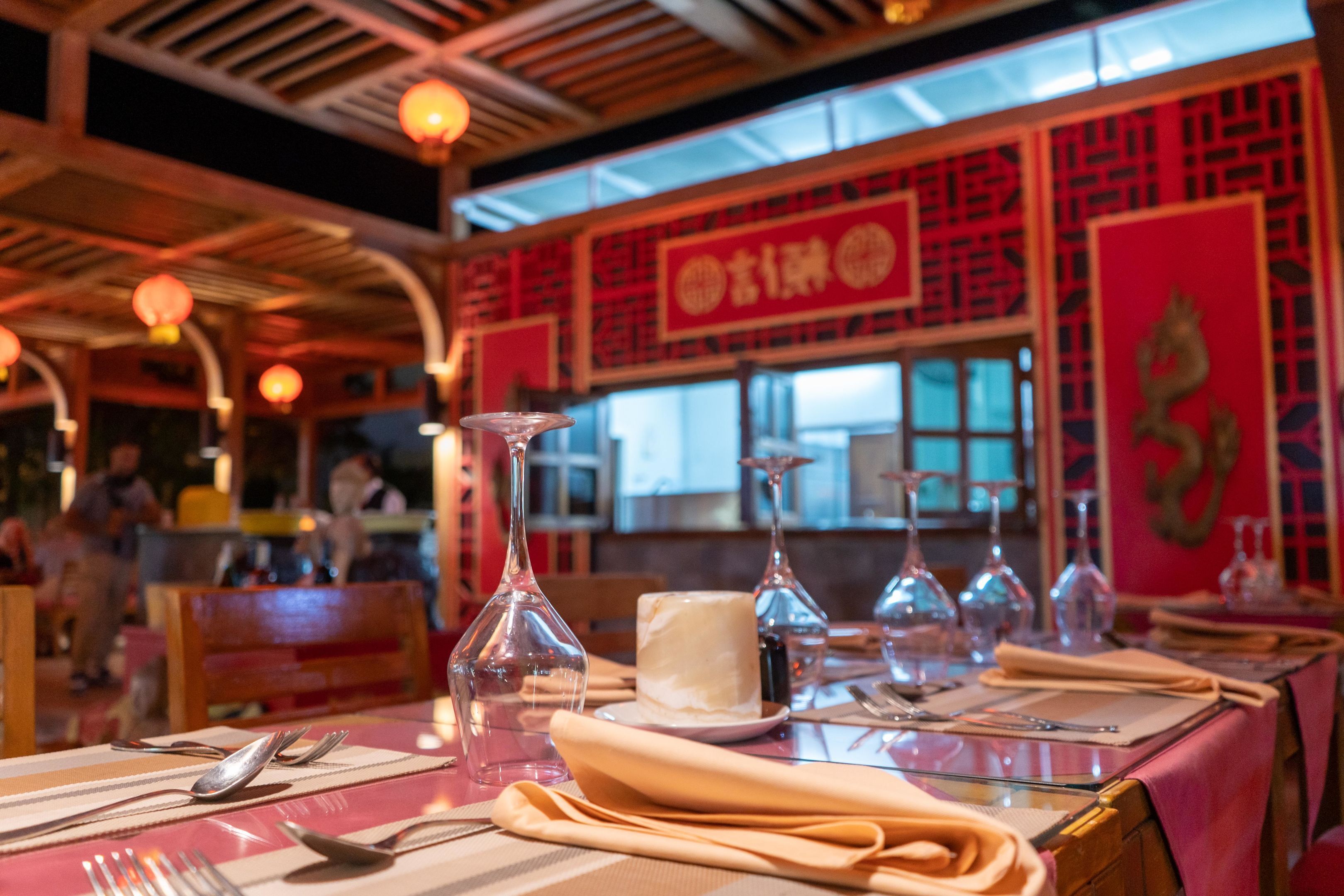L’intérieur d’un restaurant, avec des tables dressées pour le service, de la vaisselle en verre transparente et un décor traditionnel.