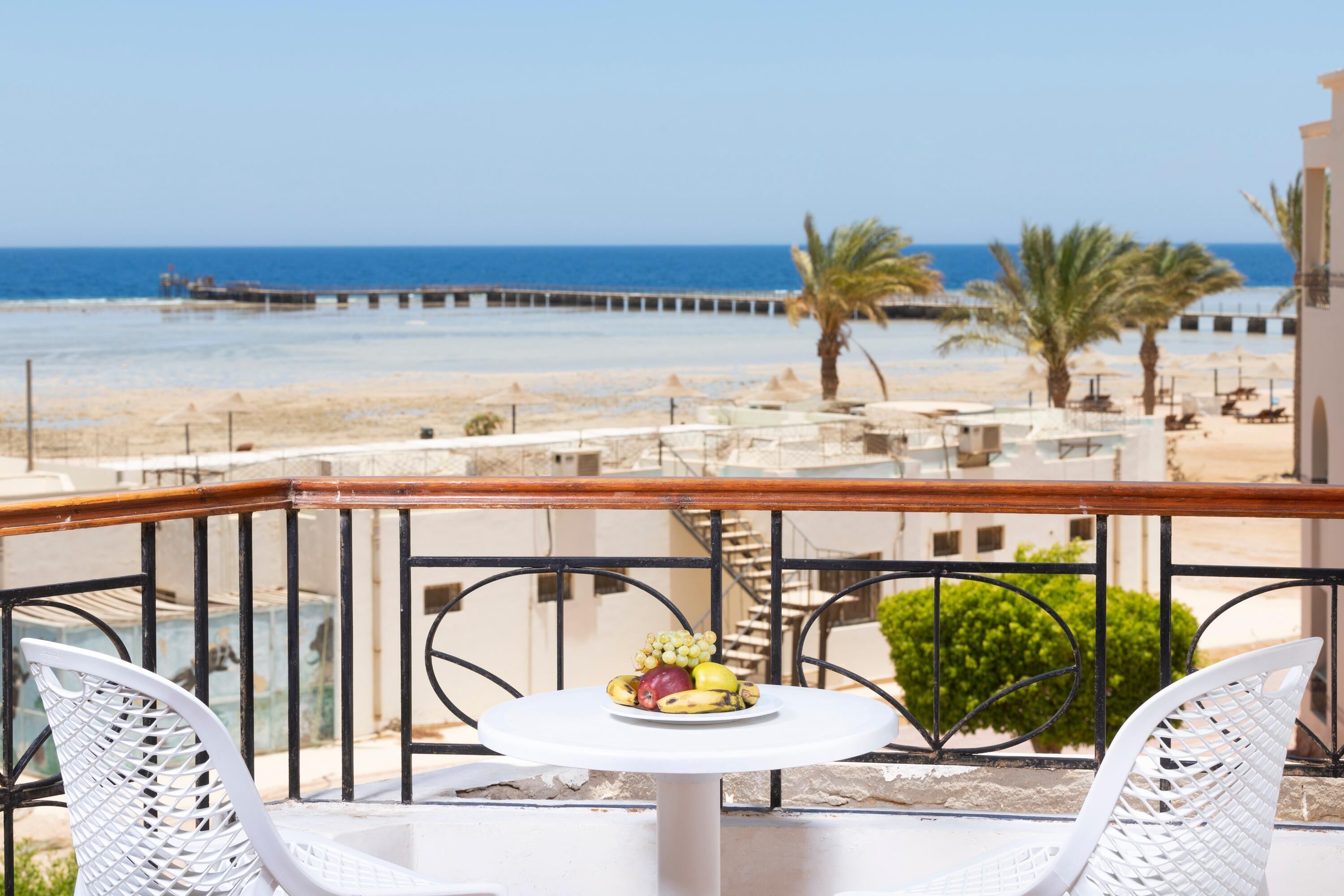 Un balcón con una mesa y sillas, con vista a una playa y palmeras.