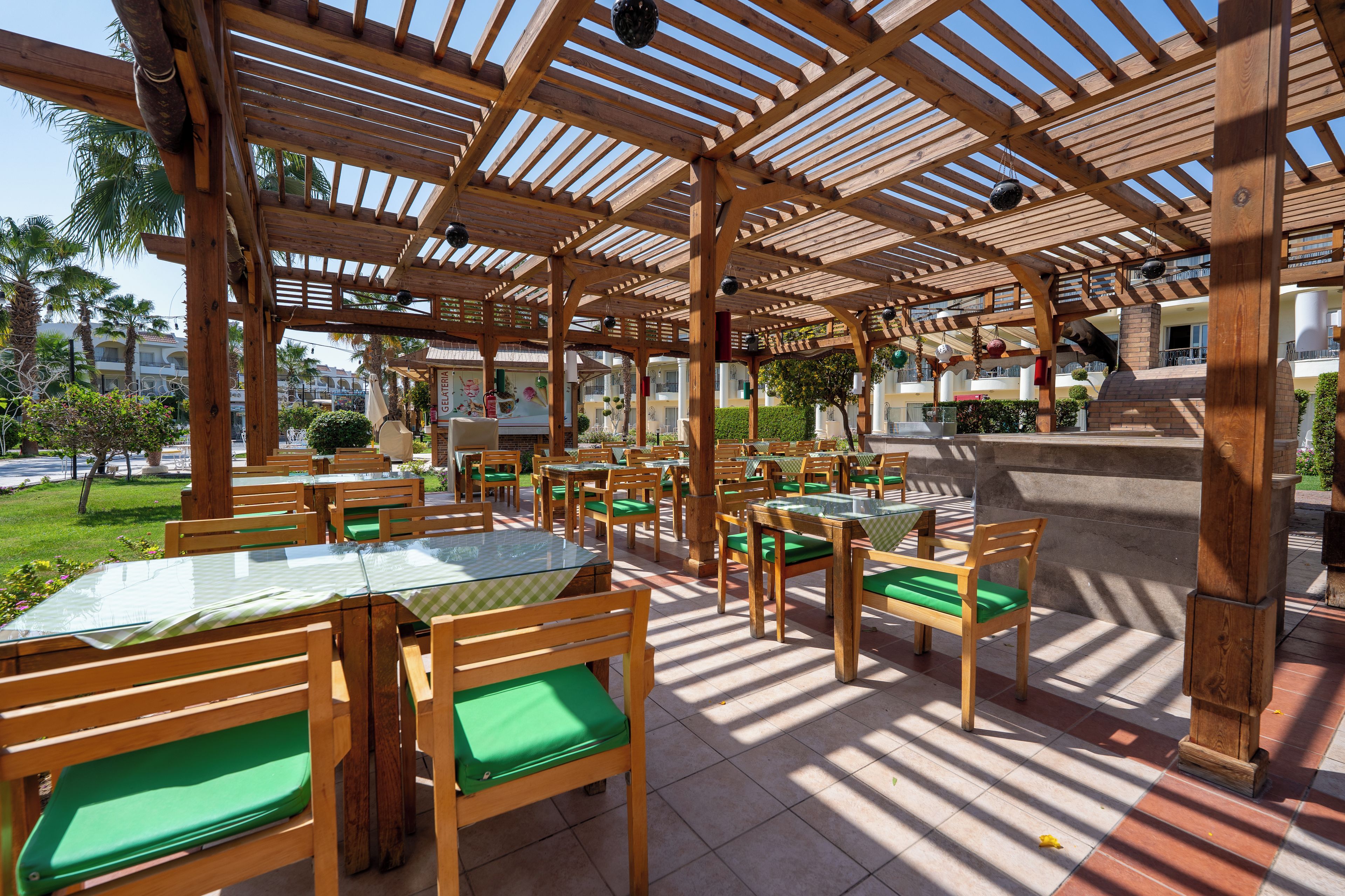 An outdoor patio area with wooden tables and chairs, covered by a wooden pergola.