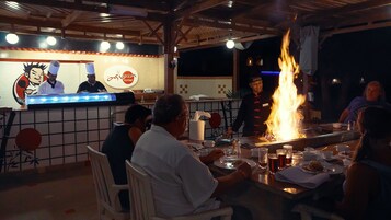 A restaurant with a sushi bar, a fire feature, and patrons dining.