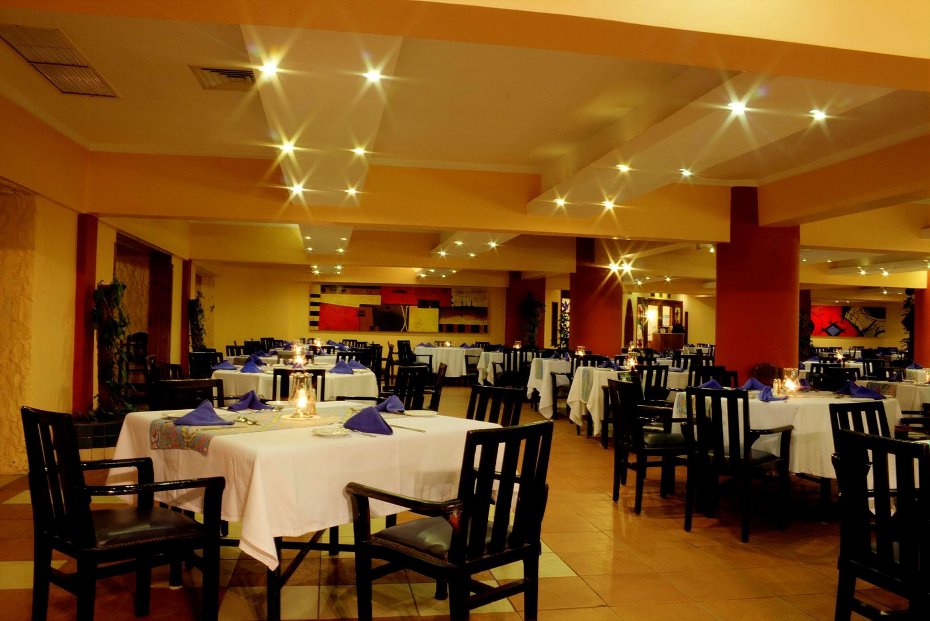 Un restaurant spacieux, doté de nombreuses tables et chaises, bien éclairé grâce à des luminaires au plafond, et offrant une atmosphère chaleureuse.