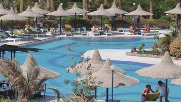 Un área de piscina con sillas de descanso y sombrillas, rodeada de palmeras y follaje.