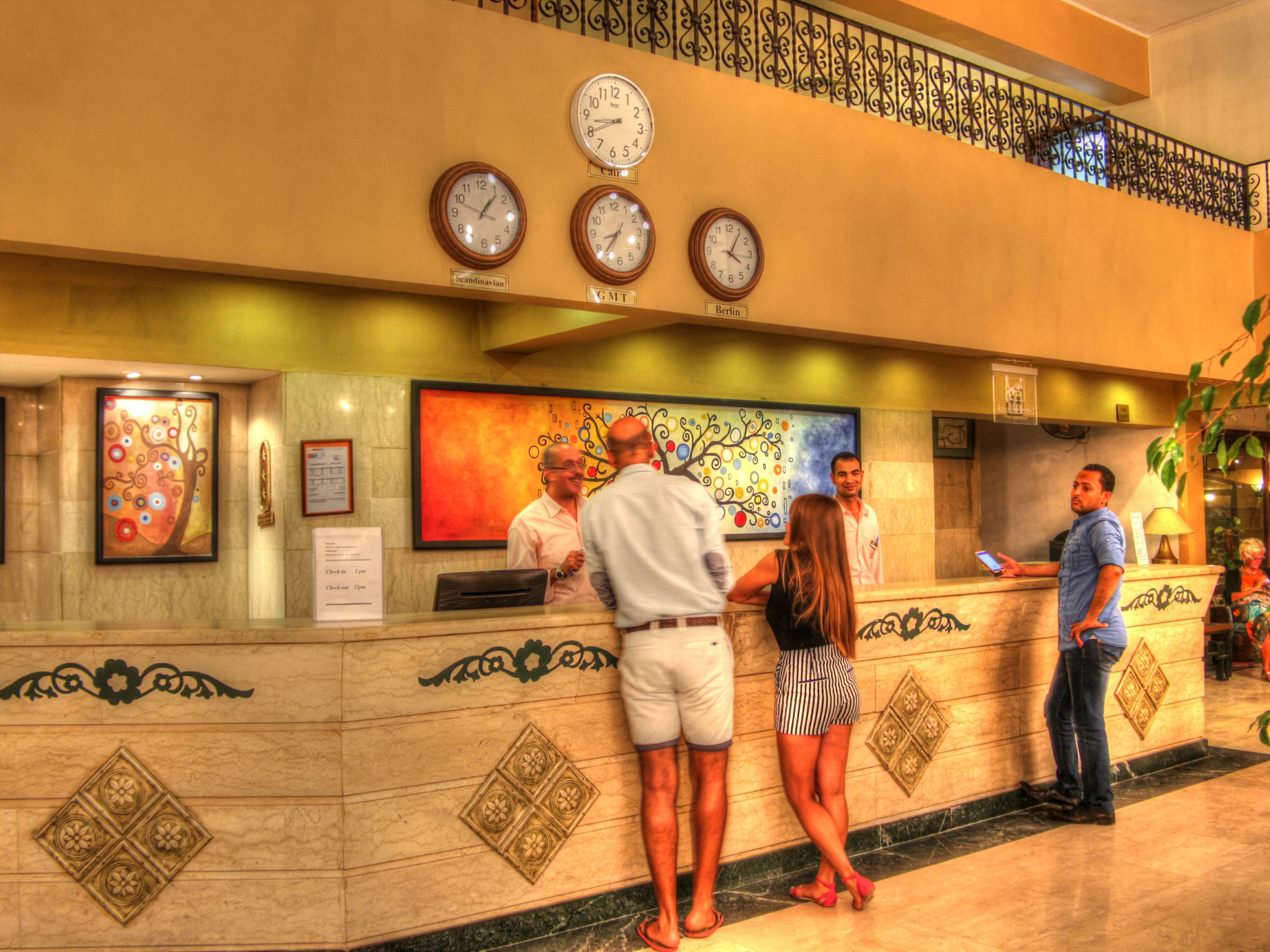 A hotel reception area with a marble counter, clocks displaying different time zones, and a large abstract painting on the wall.