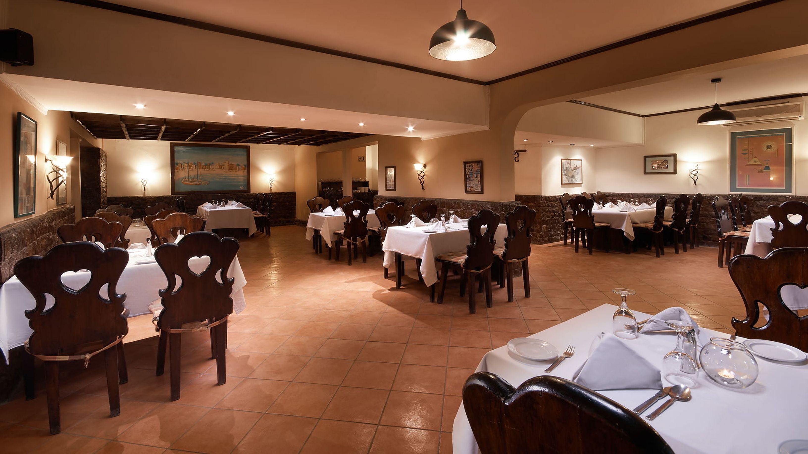 A restaurant with multiple tables and chairs, arranged in a spacious dining area with a high ceiling and warm lighting.