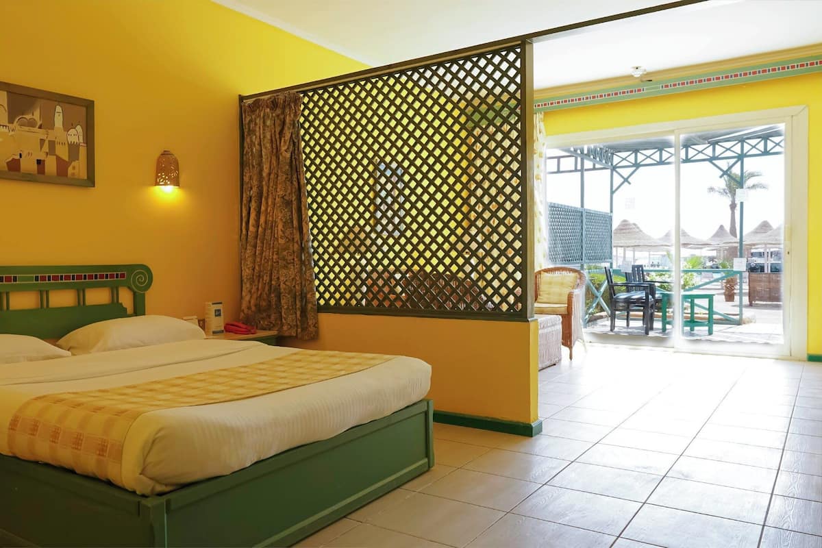 A hotel room with a bed, a nightstand, a lamp, a window with curtains, and a view of the outside.