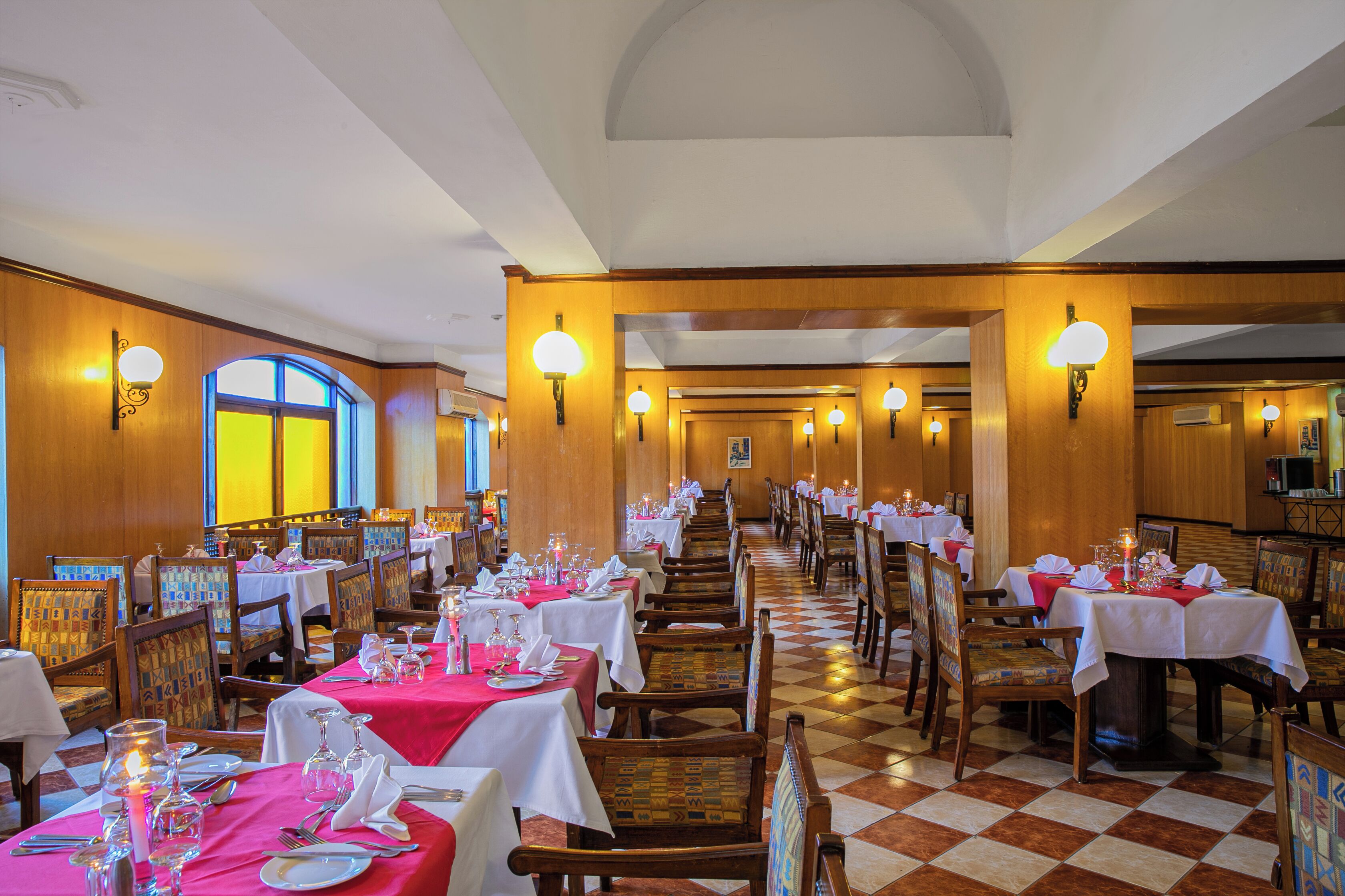 A restaurant with multiple tables set for dining, featuring a checkered floor and wooden walls.