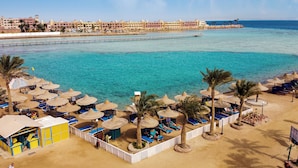A beach resort with sun loungers, umbrellas, and a view of the sea and buildings in the background. - Bel Air Azur Resort - Adults Only (Hurghada)