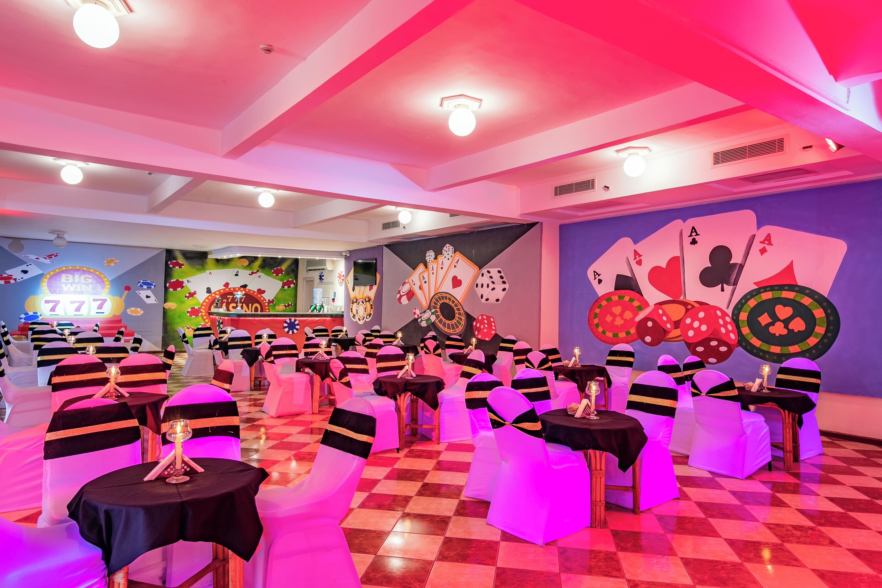 A room with tables and chairs, a stage with a DJ booth, and a wall with playing cards.