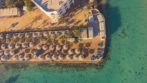 An aerial view of a beach resort with rows of sun loungers and umbrellas, a building with multiple balconies, and a clear turquoise sea. - Bel Air Azur Resort - Adults Only (Hurghada)