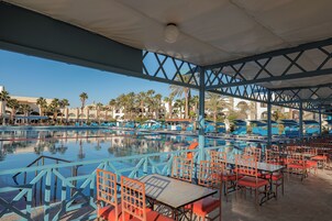Zona junto a la piscina con asientos azules y rojos, vista despejada del estanque y palmeras al fondo.