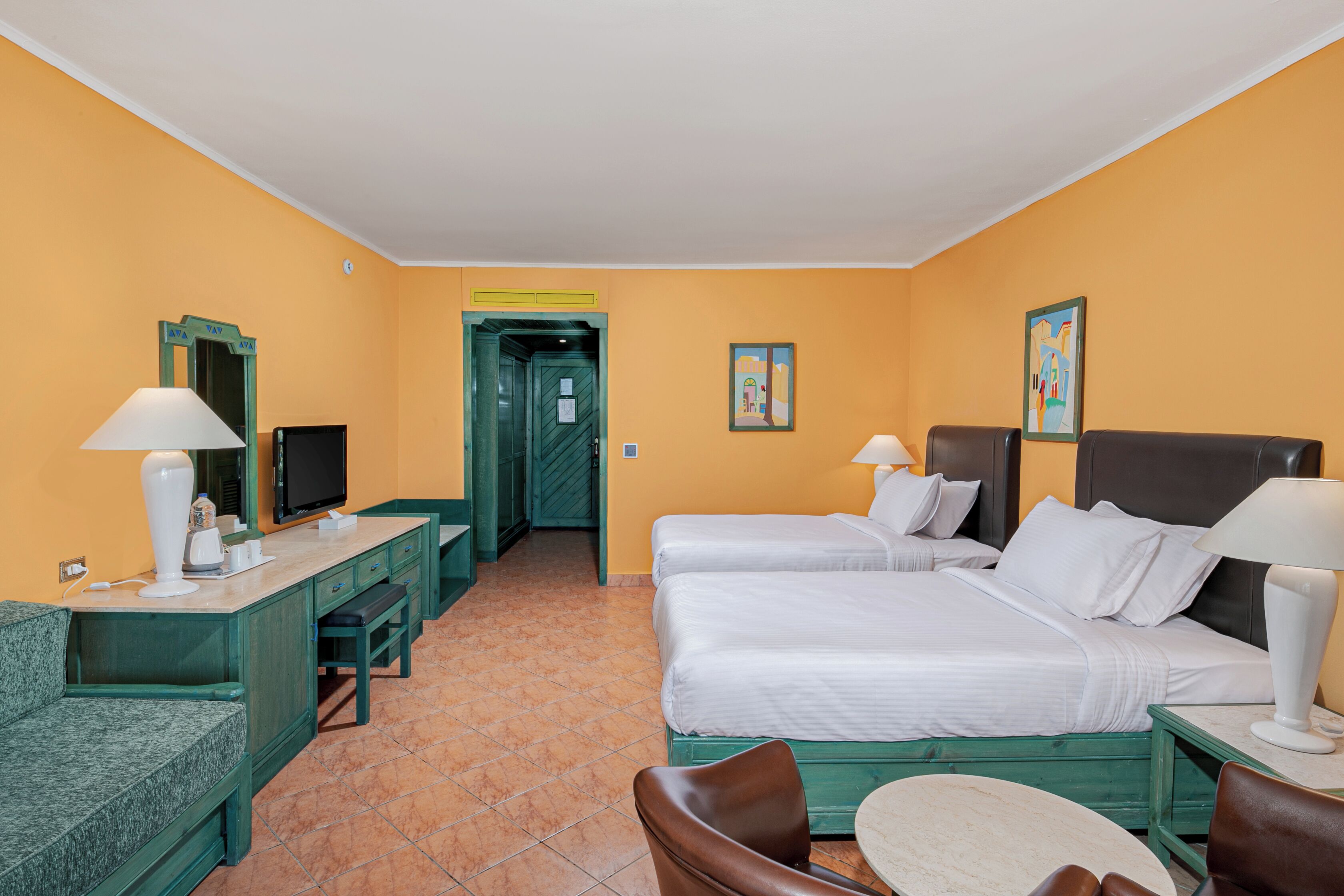 A hotel room with two beds, a desk with a chair, a TV, and a door leading to a hallway.