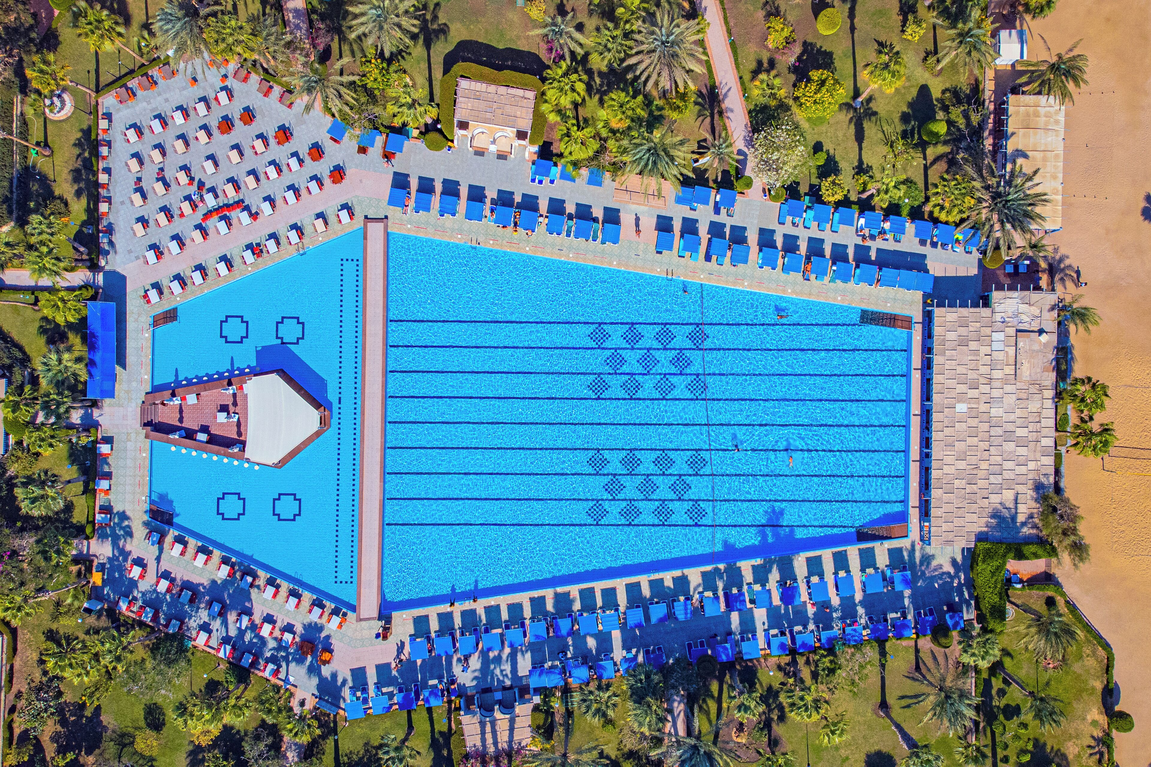 An aerial view of a hotel with a large swimming pool, multiple lounge areas, and a beachside location.