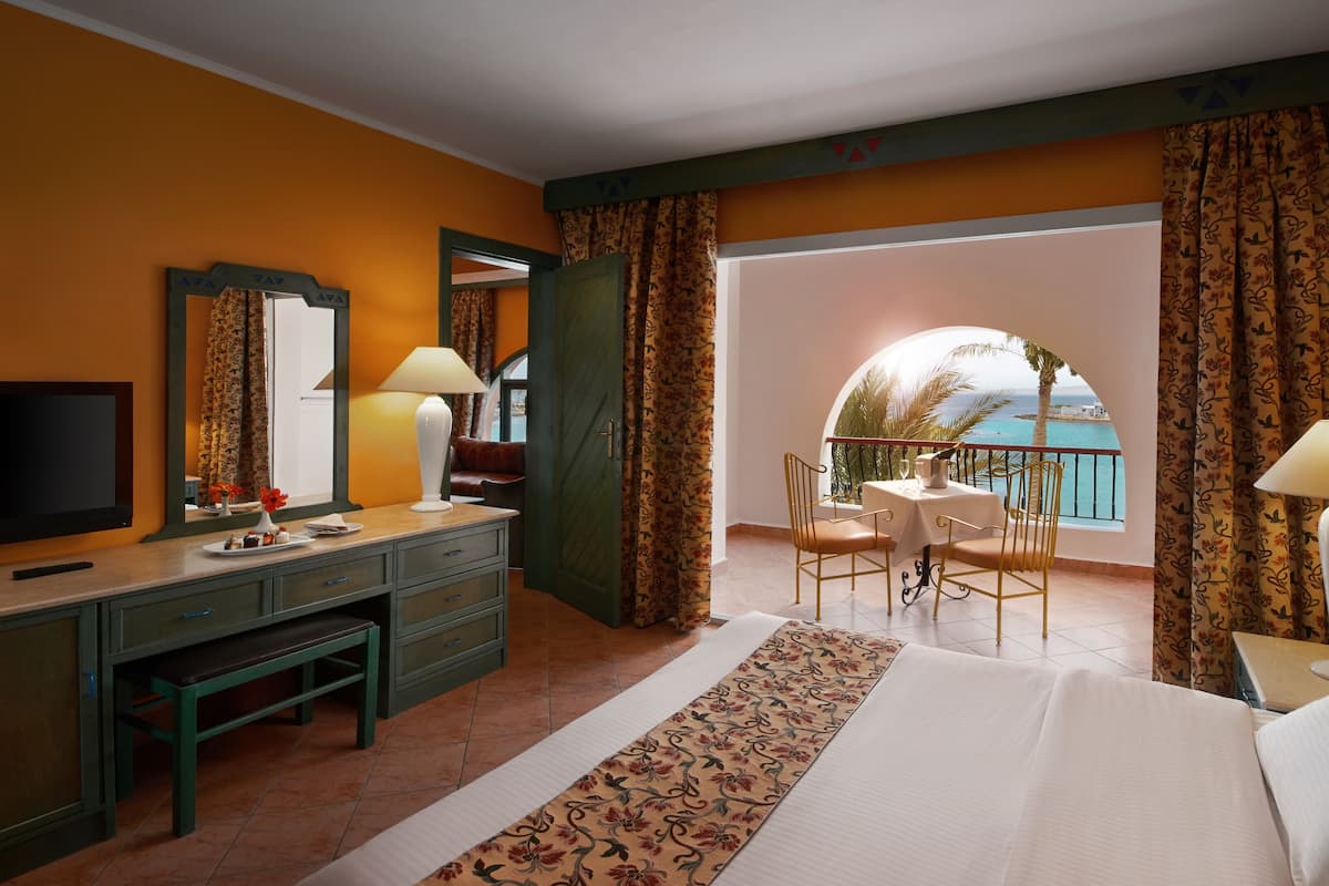 A hotel room with a bed, a desk, a TV, and a balcony with a view of the sea.