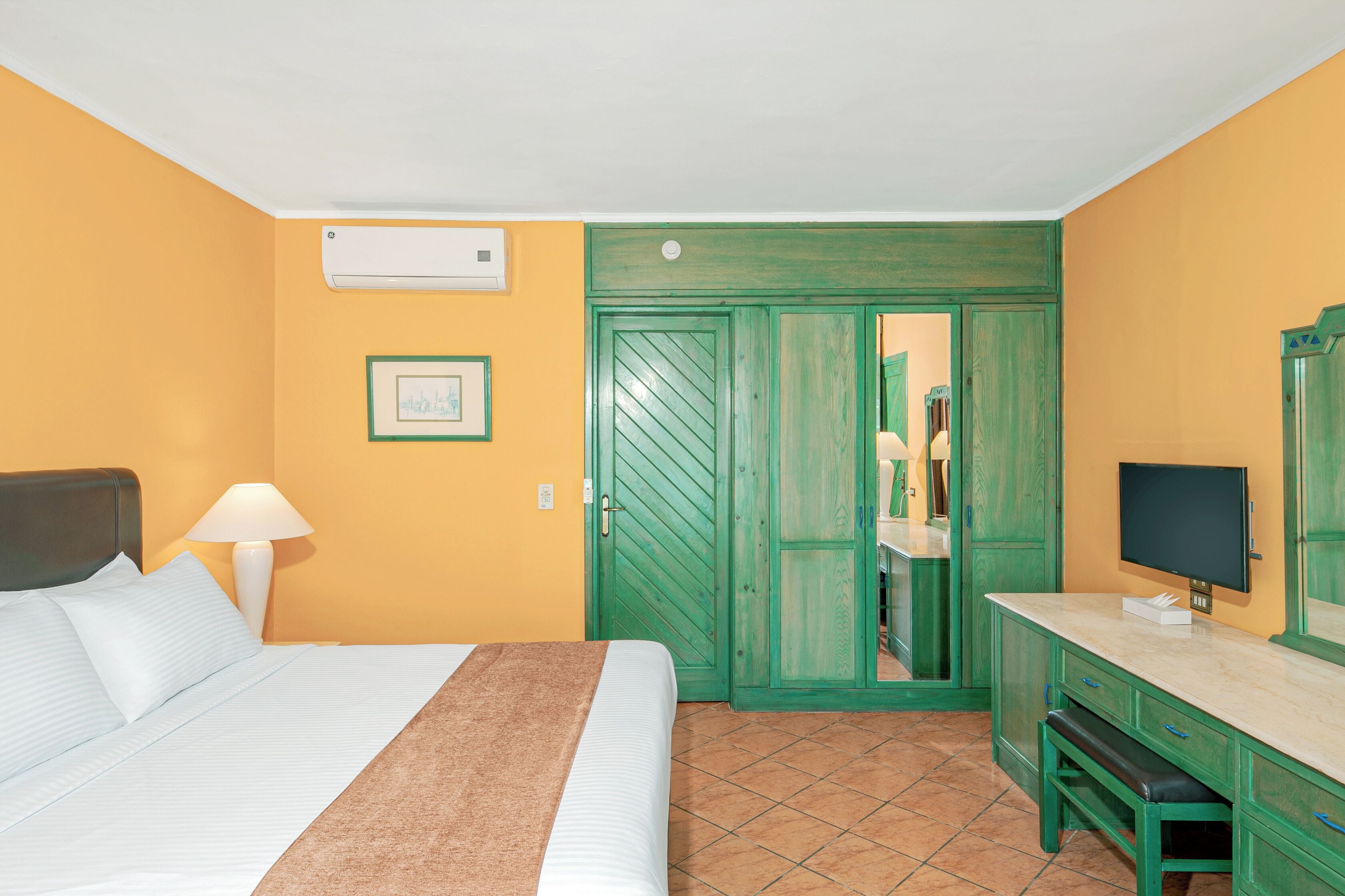 Ein Hotelzimmer mit einem Bett, einem Schreibtisch, einem Fernseher und einem grünen Kleiderschrank.