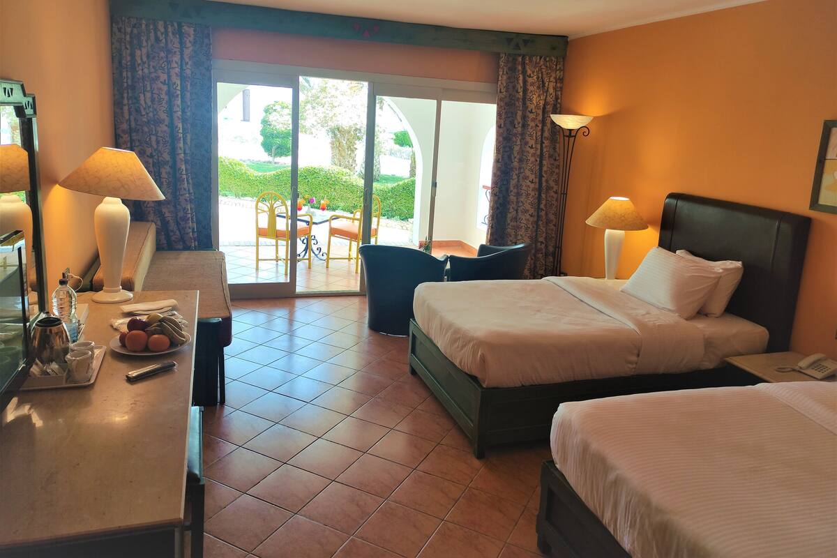 A hotel room with a bed, a desk with a lamp, a chair, and a view of the outdoors.
