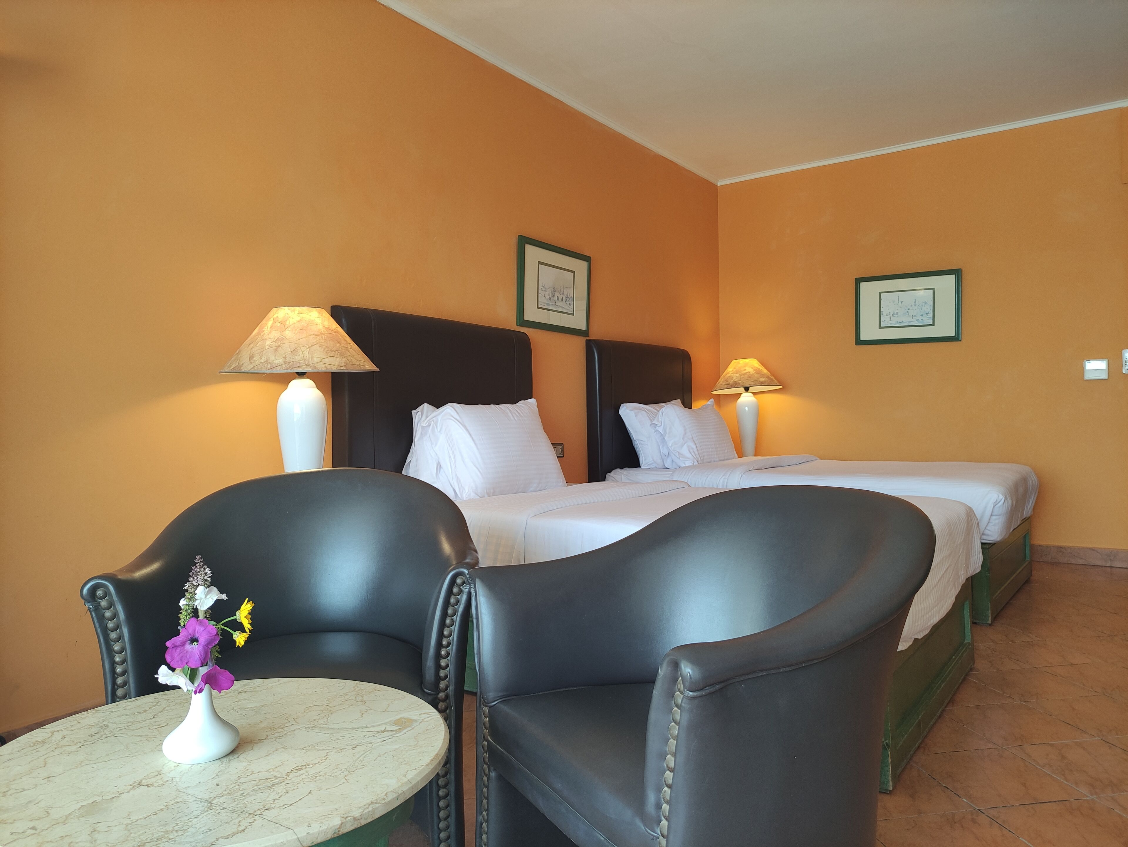 Une chambre d’hôtel avec deux lits, un coin salon avec des fauteuils et une table agrémentée d’un vase de fleurs.