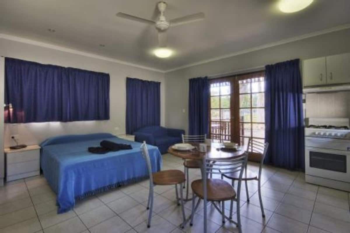 A room with a bed, a dining table with chairs, a ceiling fan, and a kitchen area.