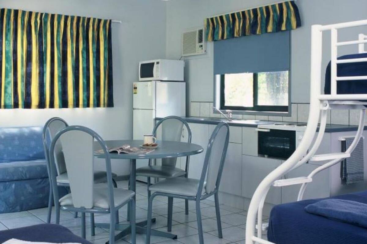A compact room with a sofa, a dining table with chairs, a kitchenette with a microwave and refrigerator, and a bunk bed with a ladder.
