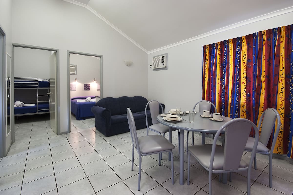 A compact room with a dining table, four chairs, a sofa, and a bunk bed.