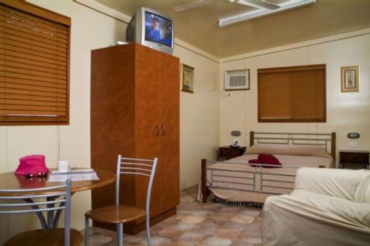 A bedroom with a bed, bedside table, chair, wardrobe, and a television on top of the wardrobe.