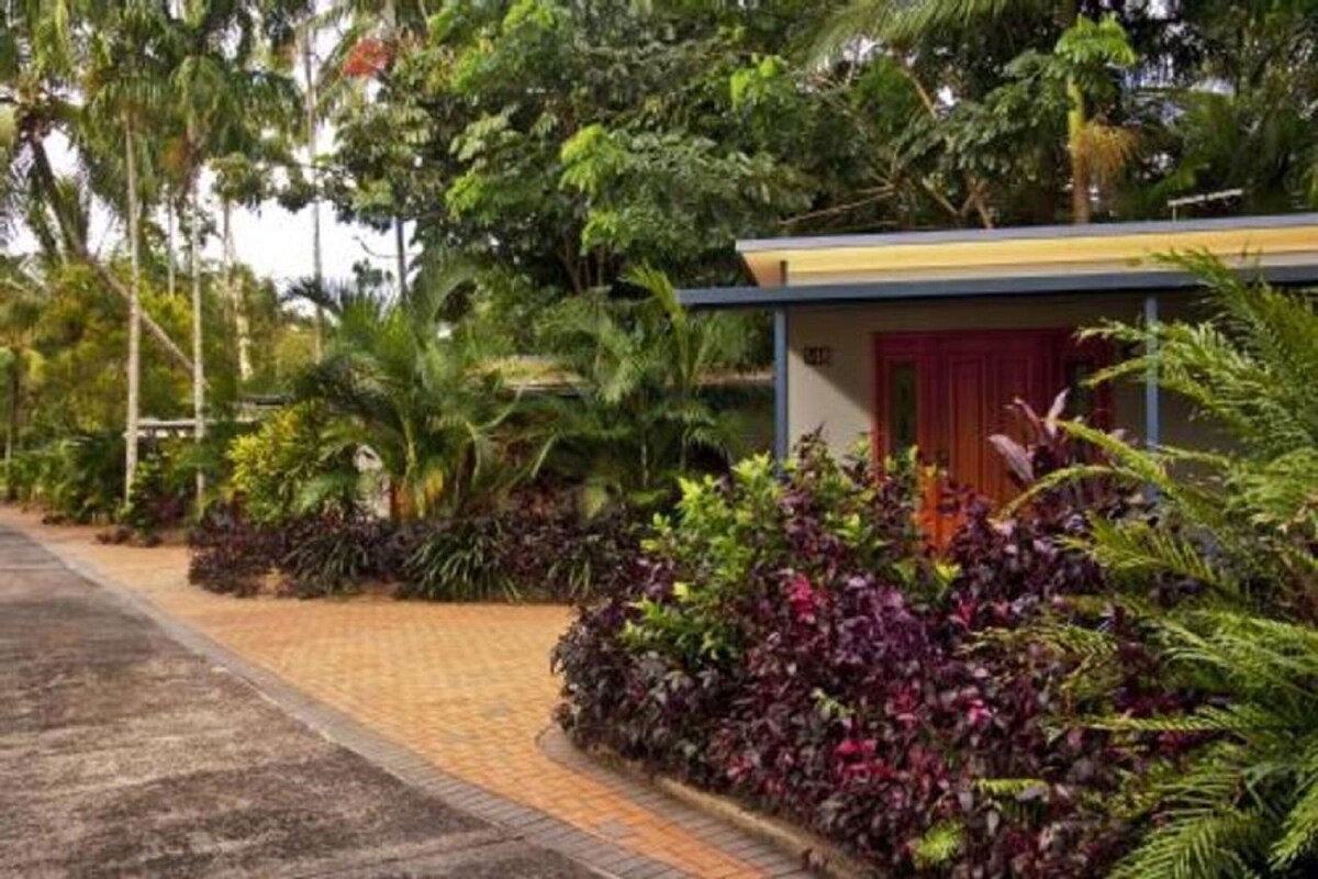A building with a red door, surrounded by lush greenery and a paved pathway.
