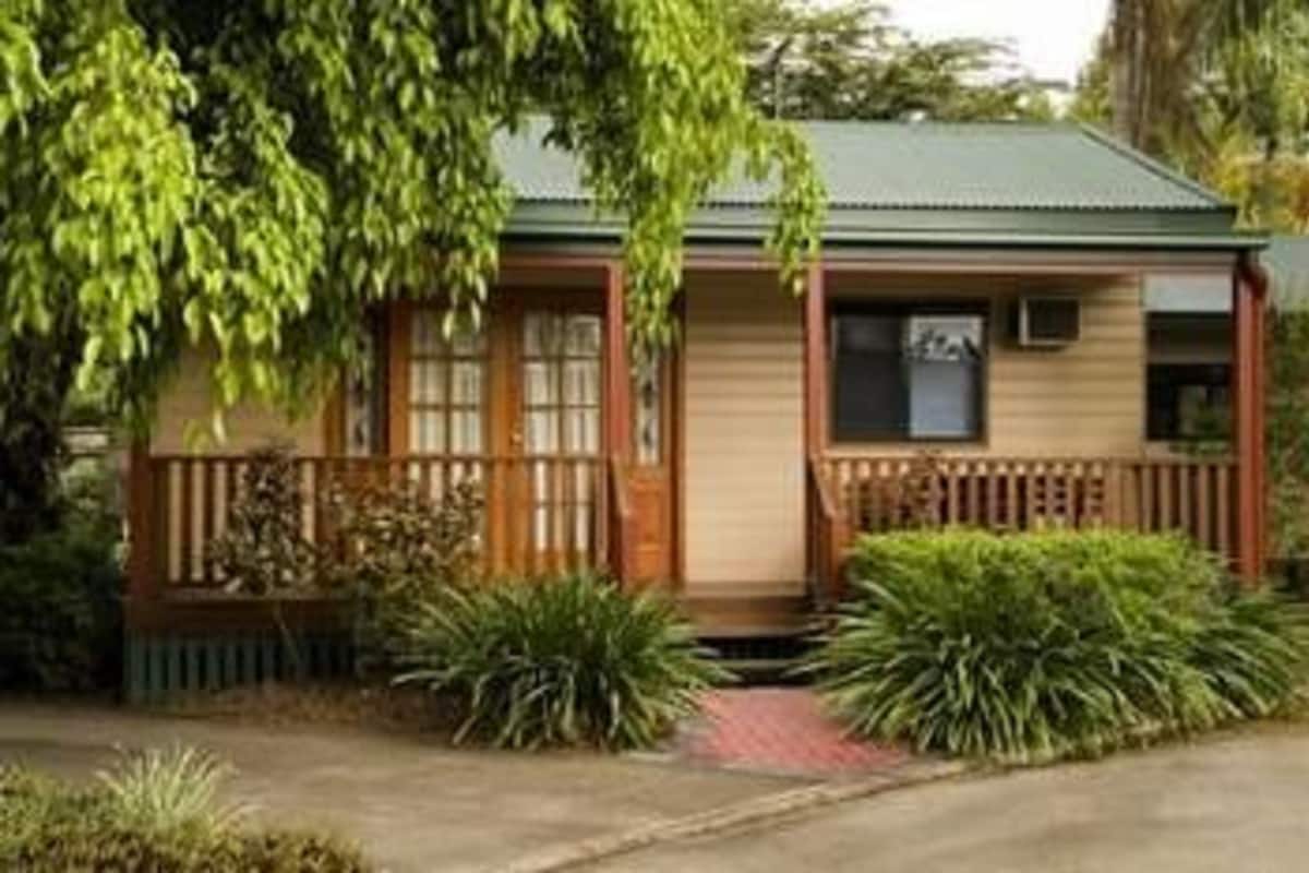 A small, single-story house with a green roof, wooden porch, and a small garden area.