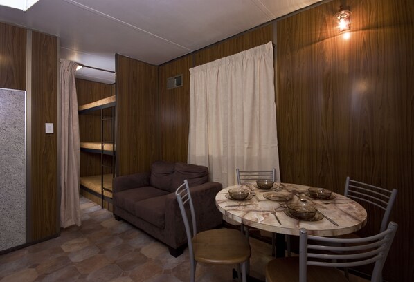 Habitación pequeña con una cama litera, un sofá, una mesa de comedor con sillas y una pared de madera.