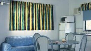 Une chambre d’hôtel de taille réduite comprenant un lit, une petite table à manger avec des chaises, un canapé, un ventilateur de plafond, un four à micro-ondes et une fenêtre avec des rideaux à rayures.