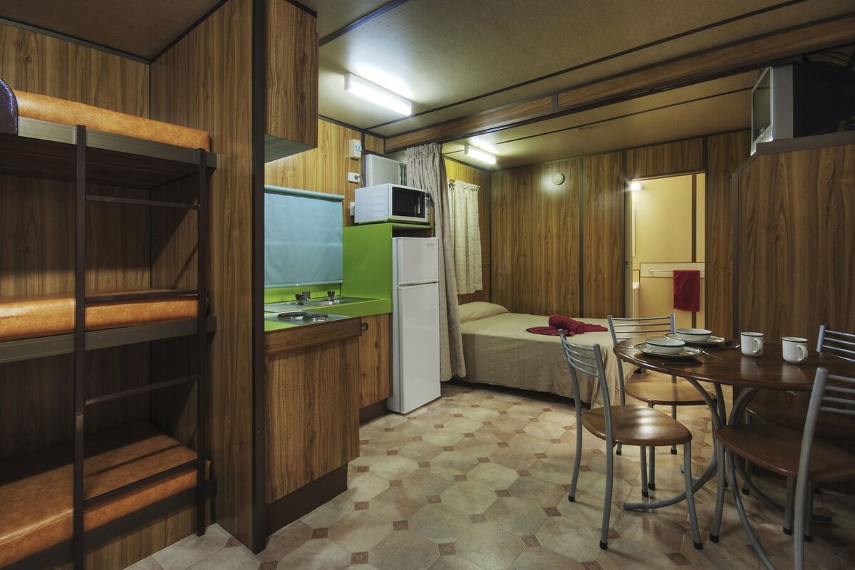 A compact kitchen with a sink, microwave, and a small refrigerator. There is a dining area with a table and chairs.