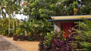 A pathway leading to a building with a red door, surrounded by lush greenery and palm trees. - Cairns Sunland Leisure Park (Manoora)