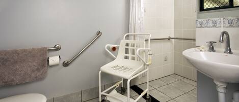 A bathroom with a toilet, a sink, a shower with a curtain, a white mobility aid, and a grab bar.