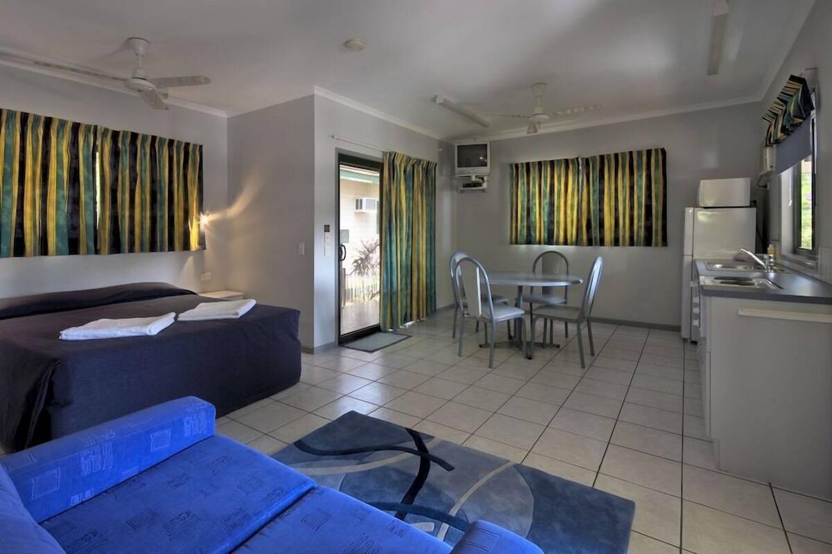 Habitación de hotel con cama, sofá, mesa de comedor con sillas, zona de cocina y ventilador de techo.