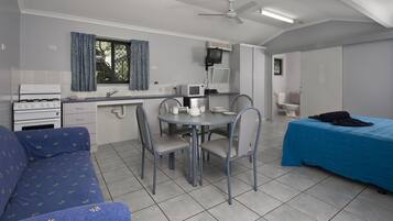 A compact room with a kitchenette, a dining table with chairs, a sofa, and a bed.