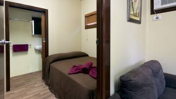 A bedroom with a bed, a wooden door, a window with blinds, a towel rack, and a wall-mounted air conditioner.