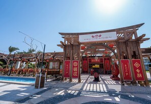 A traditional Chinese architectural entrance with a wooden archway, a signboard, and red banners. - JAZ Royal Palmariva (Makadi Bay)