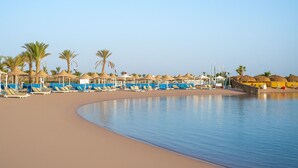 A beach with sun loungers and umbrellas, a pool, and palm trees. - JAZ Royal Palmariva (Makadi Bay)