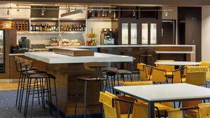 A modern bar area with a central island, bar stools, yellow chairs, and a coffee machine.