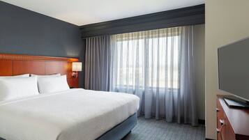 Habitación de hotel con una cama grande, un televisor de pantalla plana, un cabecero de madera y una ventana con cortinas translúcidas.