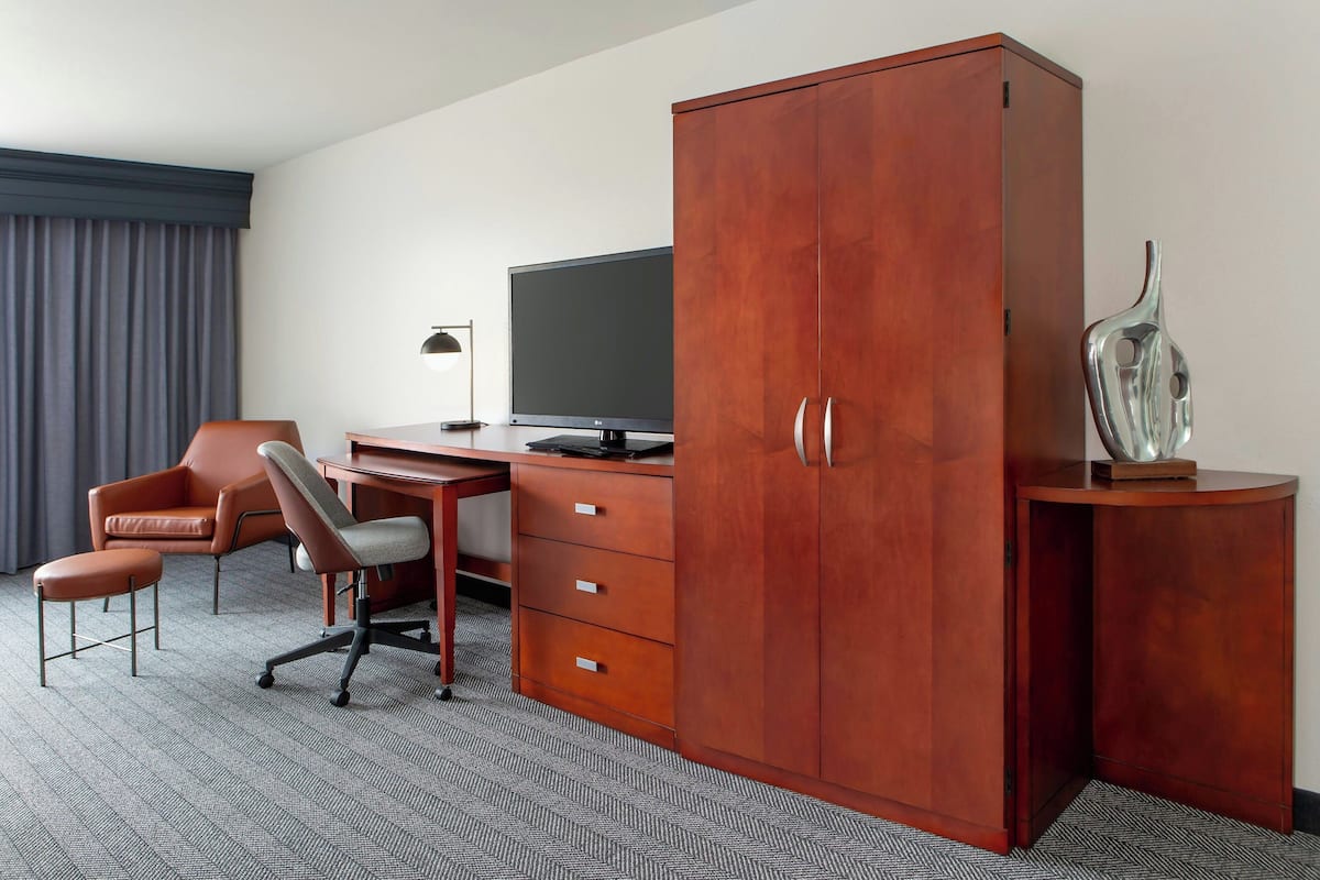 Ein Hotelzimmer mit einem Holztisch, einem Fernseher, einem Sessel und einem Schrank.