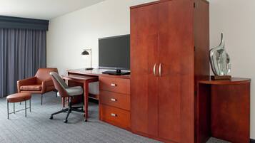 Quarto de hotel com escrivaninha de madeira, televisão, cadeira e armário.