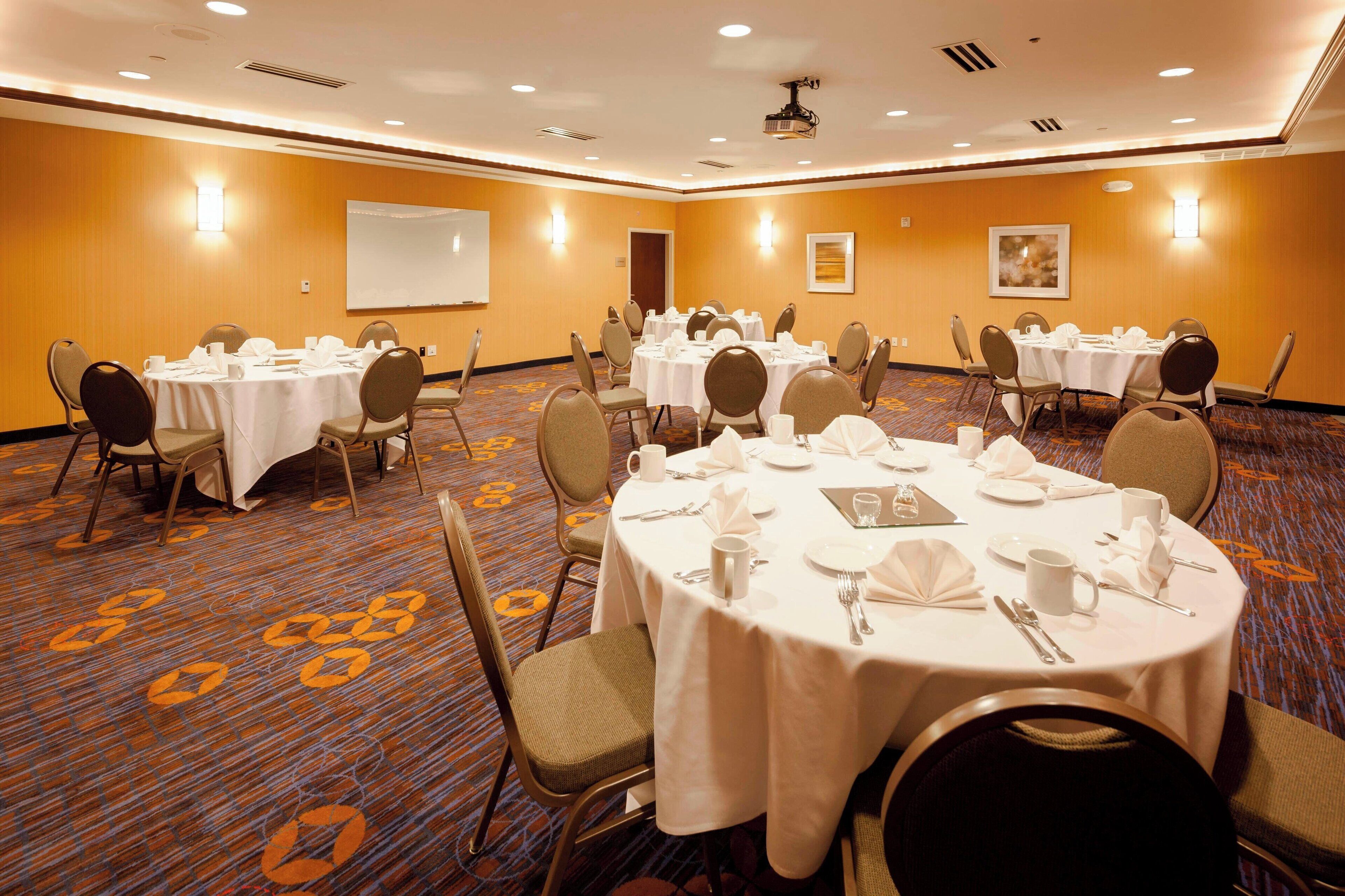 Un salón de conferencias con varias mesas redondas, cada una con mantel blanco, sillas y cubiertos.