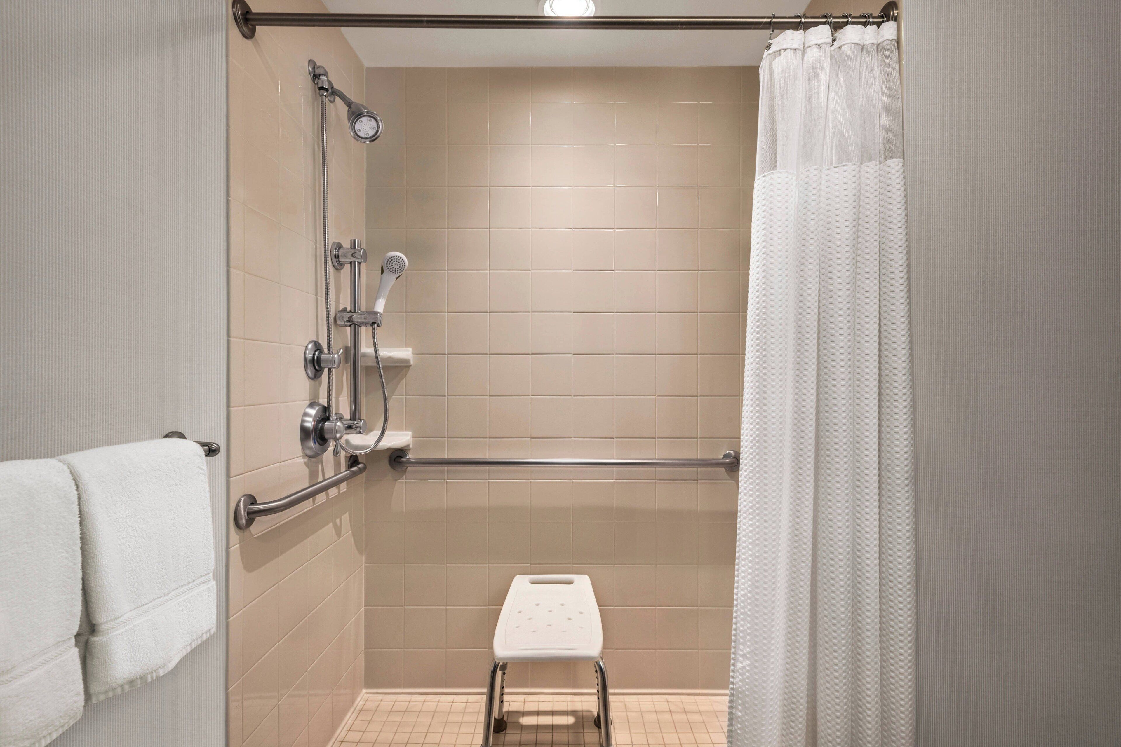 A shower area with a handheld showerhead, a handheld shower attachment, a grab bar, and a white step stool.