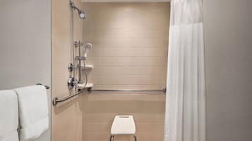 A shower area with a handheld showerhead, a handheld shower attachment, a grab bar, and a white step stool.