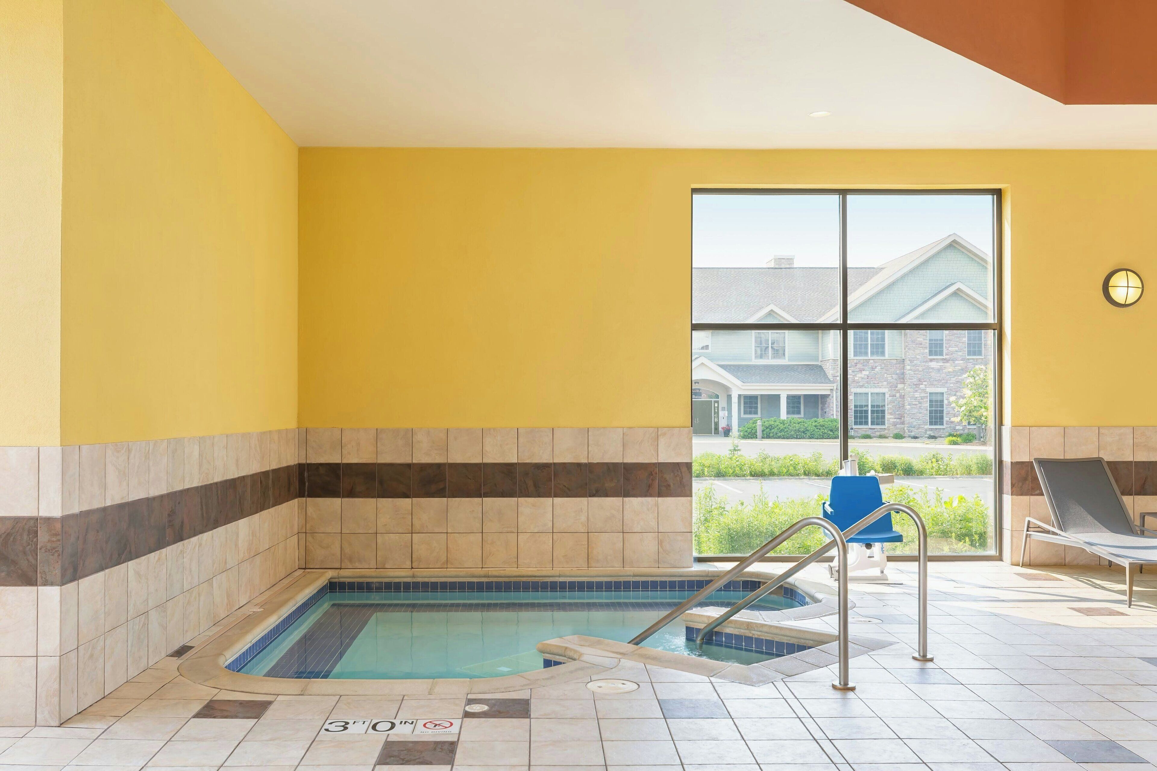A pool area with a 3-foot depth marker, a window with a view of buildings, and a blue chair.
