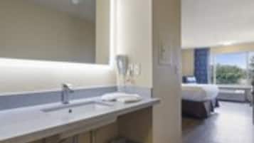 A modern bathroom with a large mirror, a sink, and a trash bin.